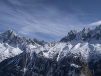 a mountain range with snow on top and some clouds in the background and a bright blue sky overhead