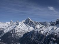 a mountain range with snow on top and some clouds in the background and a bright blue sky overhead