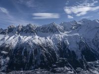 a mountain range with snow on top and some clouds in the background and a bright blue sky overhead