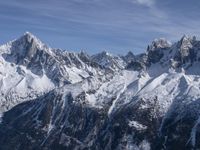 a mountain range with snow on top and some clouds in the background and a bright blue sky overhead