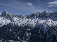 a mountain range with snow on top and some clouds in the background and a bright blue sky overhead