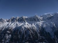 a mountain range with snow on top and some clouds in the background and a bright blue sky overhead