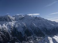 a mountain range with snow on top and some clouds in the background and a bright blue sky overhead