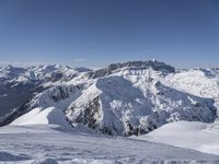 snow covered mountains and hills with a skier standing on the top of the hill, looking down