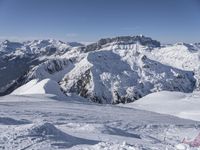 snow covered mountains and hills with a skier standing on the top of the hill, looking down