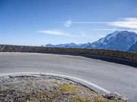 a curve in the road of the mountain range with snow capped mountains and a blue sky