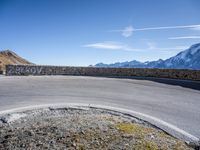 a curve in the road of the mountain range with snow capped mountains and a blue sky