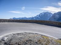 a curve in the road of the mountain range with snow capped mountains and a blue sky