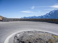 a curve in the road of the mountain range with snow capped mountains and a blue sky