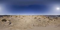 a panoramic view of an area in the daytime with a desert, mountains and distant sun