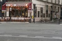 a cafe sits in an intersection beside a traffic light and a sidewalk with chairs and umbrellas