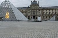 a glass and silver pyramid in front of a building and fountain in the middle of a courtyard