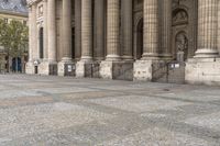 a woman is holding a umbrella while walking by some pillars and a building with pillars