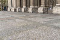 a woman is holding a umbrella while walking by some pillars and a building with pillars