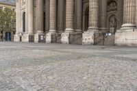 a woman is holding a umbrella while walking by some pillars and a building with pillars