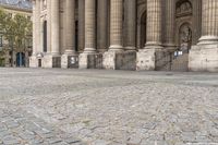 a woman is holding a umbrella while walking by some pillars and a building with pillars