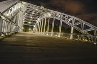 a large bridge with a man walking across it at night time in the city with some lights