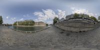 the fish - eye lens is shown of a stone wall surrounding a river, buildings and bridge