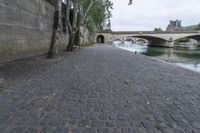 the walkway between two bridges is set along a river in paris, france, on a cloudy day