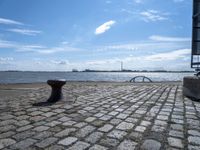 a park bench sitting by the water and water in the distance under a blue sky