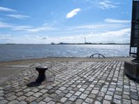 a park bench sitting by the water and water in the distance under a blue sky