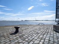 a park bench sitting by the water and water in the distance under a blue sky