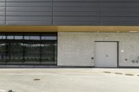 a parking area with two parked cars in front of it and three doors with pots on either side of the building