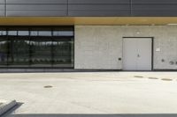 a parking area with two parked cars in front of it and three doors with pots on either side of the building