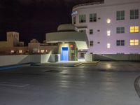 a parking lot with an entrance lit up at night in an apartment complex that also serves as a parking garage