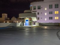 a parking lot with an entrance lit up at night in an apartment complex that also serves as a parking garage