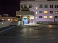 a parking lot with an entrance lit up at night in an apartment complex that also serves as a parking garage