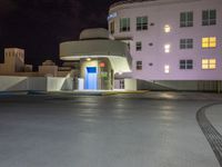 a parking lot with an entrance lit up at night in an apartment complex that also serves as a parking garage