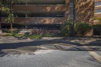 the street is empty but the buildings are lined with brick faced windows, a stop sign and a large parking garage