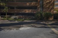 the street is empty but the buildings are lined with brick faced windows, a stop sign and a large parking garage