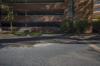 the street is empty but the buildings are lined with brick faced windows, a stop sign and a large parking garage