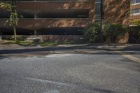 the street is empty but the buildings are lined with brick faced windows, a stop sign and a large parking garage