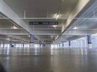 an empty parking garage with only two signs above it and cars parked nearby and on the side