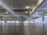 an empty parking garage with only two signs above it and cars parked nearby and on the side