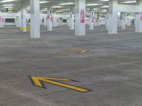 an empty parking garage with arrow painted on the floor and yellow arrows pointing left into the direction of an exit sign