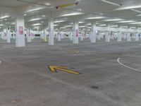 an empty parking garage with arrow painted on the floor and yellow arrows pointing left into the direction of an exit sign