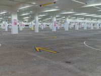 an empty parking garage with arrow painted on the floor and yellow arrows pointing left into the direction of an exit sign