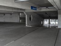 a parking garage with cement flooring and large metal poles, near some windows and light