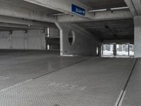 a parking garage with cement flooring and large metal poles, near some windows and light