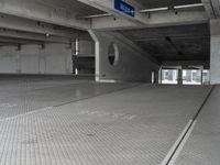 a parking garage with cement flooring and large metal poles, near some windows and light