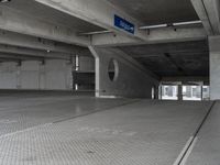 a parking garage with cement flooring and large metal poles, near some windows and light