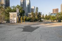 a parking lot with a trash can and a bench in front of a city skyline