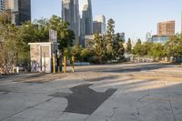 a parking lot with a trash can and a bench in front of a city skyline