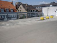a parking lot with yellow and red cars parked on the road, a blue fence, and other houses