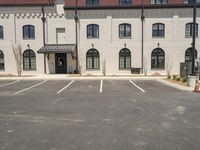 a parking lot with a brick building behind it and buildings in the background with small trees