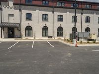 a parking lot with a brick building behind it and buildings in the background with small trees